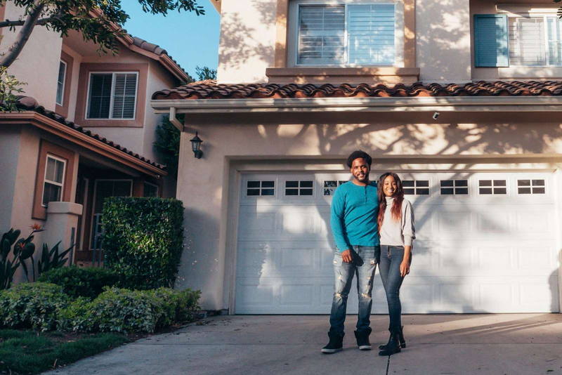 Una pareja joven de pie frente a la casa que acaban de comprar.