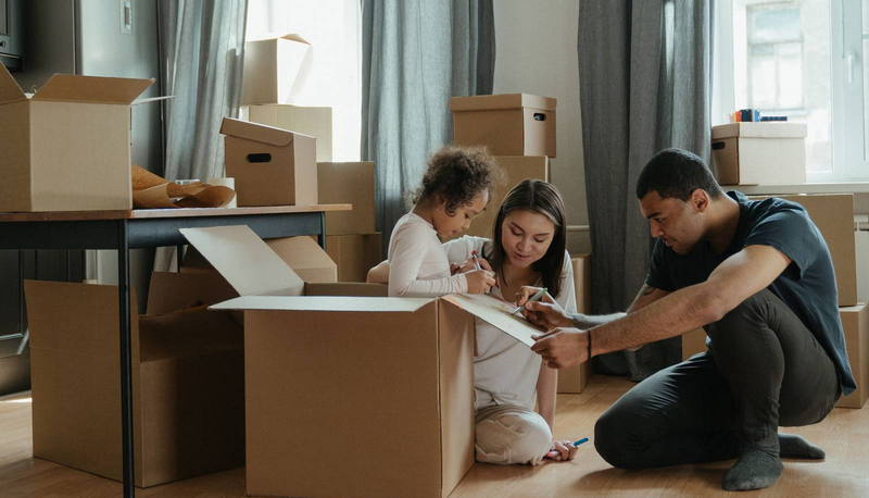 Una familia con su hija pequeña empacando cajas de mudanza en el piso de la sala.
